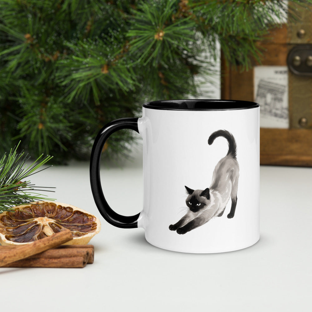 Stretching Siamese cat mug with black interior on a festive holiday table, handle on left
