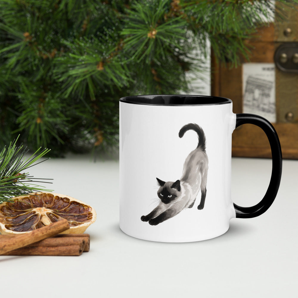 Stretching Siamese cat mug with black interior on a festive holiday table, handle on right