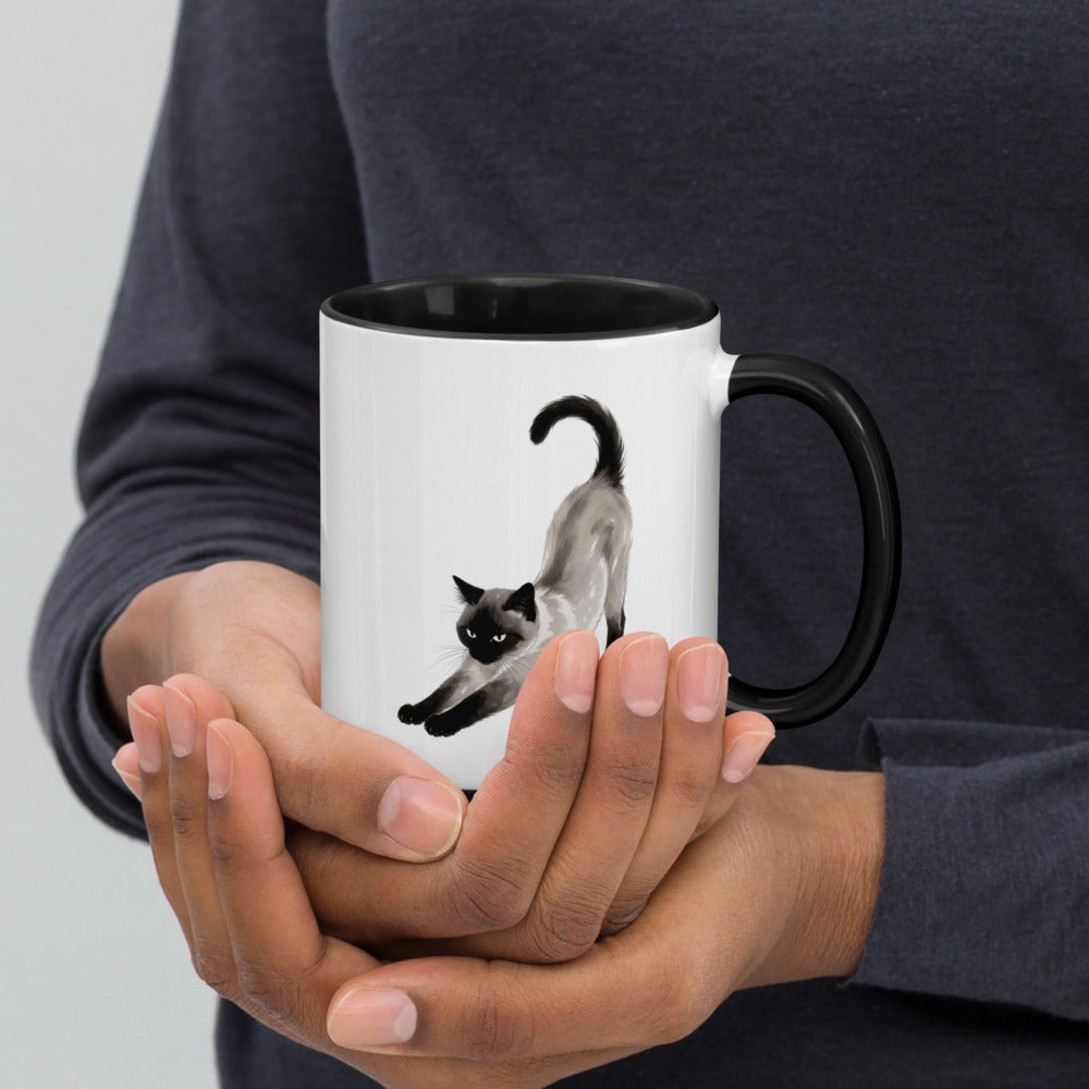 Hands holding the Stretching Siamese cat mug with black interior, handle on right